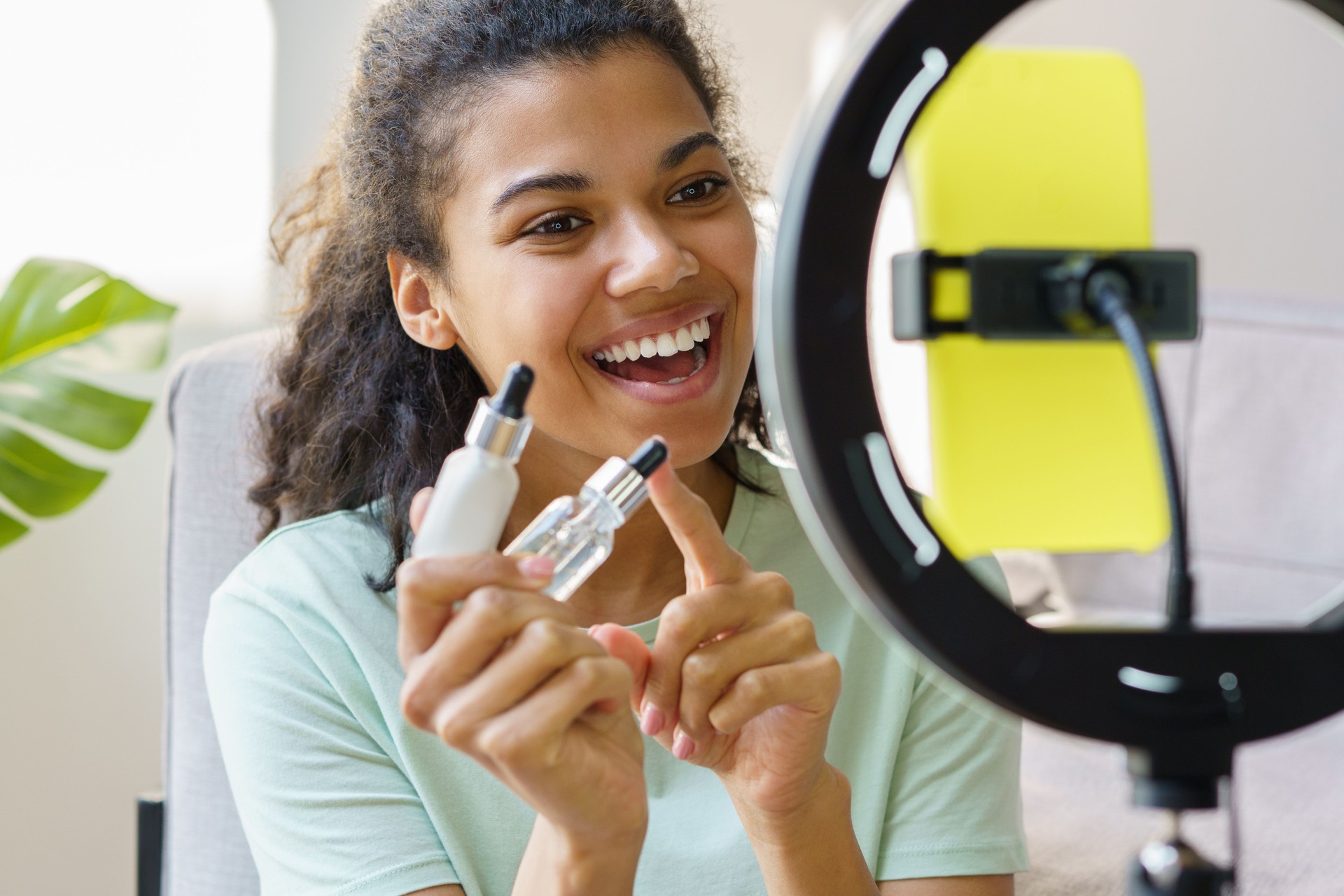 Smiling African American beauty influencer holding serum bottle communication with subscribers, recording video at home